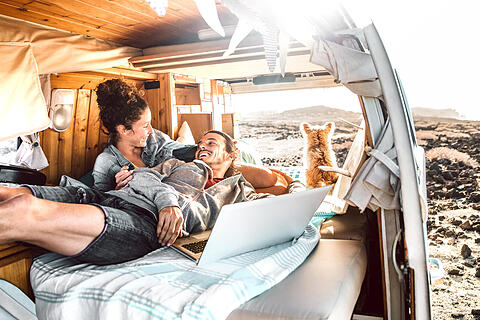 Hipster couple with dog traveling together on retro mini van transport - Digital nomad concept with indie people on minivan romantic trip working at laptop pc in relax moment - Warm contrast filter